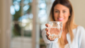 Beautiful young woman smiling while holding a glass of water at home. Lifestyle concept.