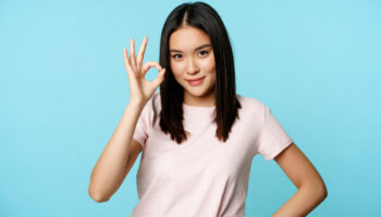 Smiling asian woman showing okay sign, gives approval, recommends smth good, standing over blue background